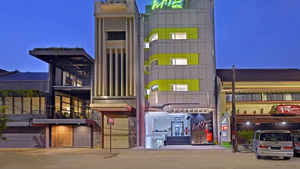 Un hotel de diseño moderno, con un llamativo letrero 'WHIZ HOTEL', una fachada curva y una entrada visible con una escalera que conduce a la recepción.