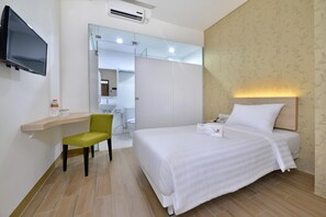 Une chambre d’hôtel avec un lit, un bureau et une chaise, un téléviseur et une salle de bain visible à travers une porte ouverte.