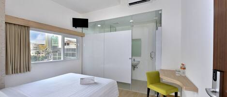 Ein Hotelzimmer mit Bett, Sessel, Schreibtisch mit Computer, Badezimmer mit Waschbecken und einem an der Wand befestigten Fernseher.