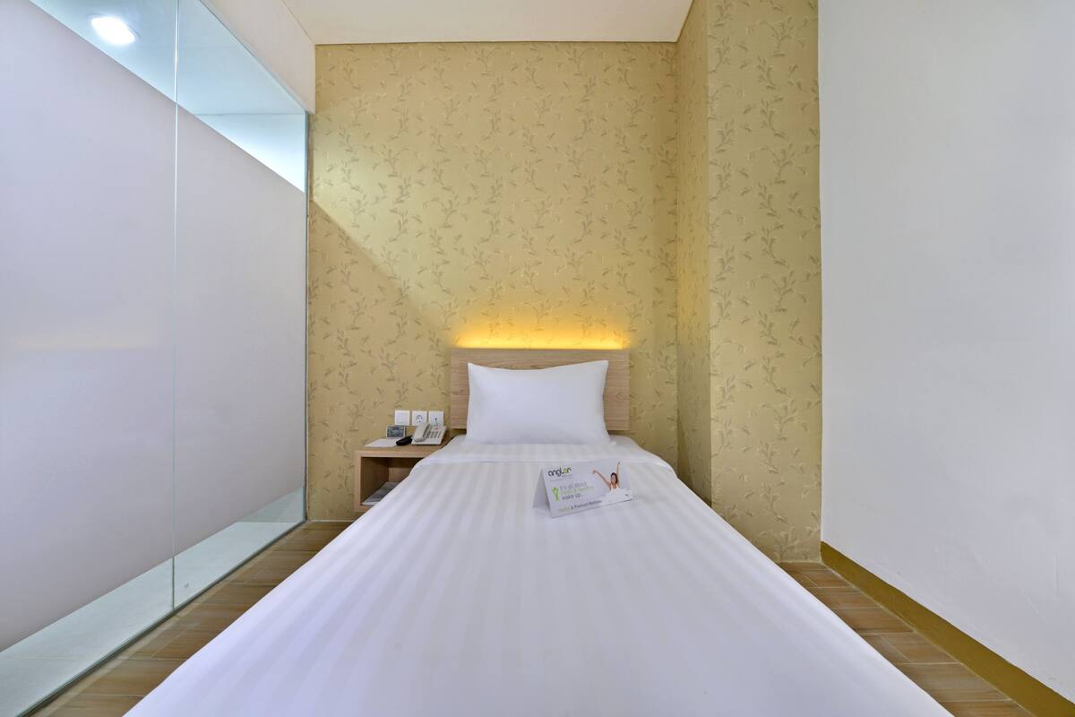A hotel room with a neatly made bed, a bedside table with a phone, and a wall with a floral pattern.