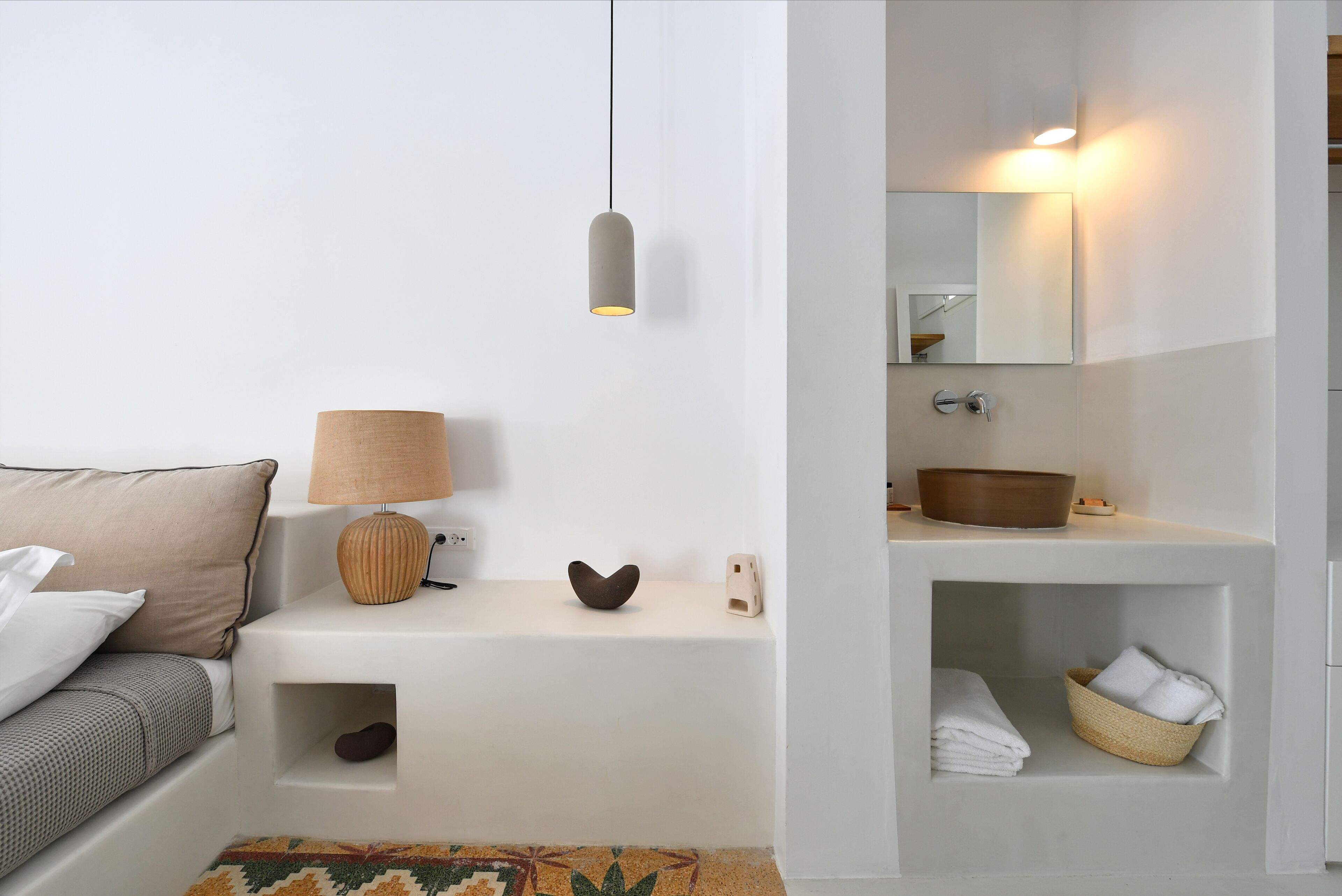 A modern bathroom with a white vanity, a mirror, a hanging light, and a towel basket.