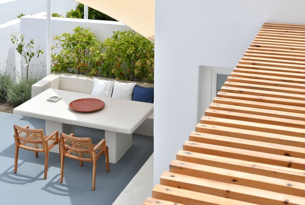 Un espacio exterior moderno con una mesa blanca, sillas de mimbre y una estructura de madera con listones.