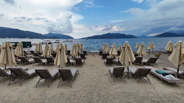 A beach with rows of sun loungers and umbrellas, a calm sea, and distant mountains.