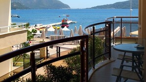 A balcony with a view of the sea, outdoor seating, and a boat docked nearby.