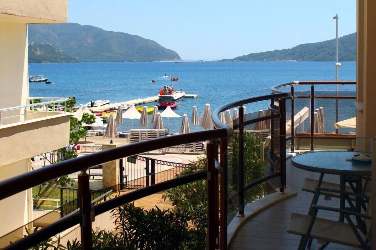 A balcony with a view of the sea, outdoor seating, and a boat docked nearby.
