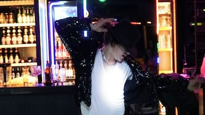 A person standing in a dimly lit area with a bar in the background.