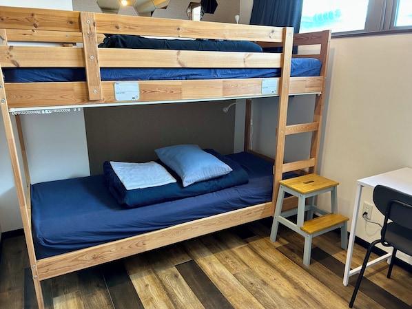 Una cama litera con escritorio y silla, un taburete de madera pequeño y una ventana con cortinas.