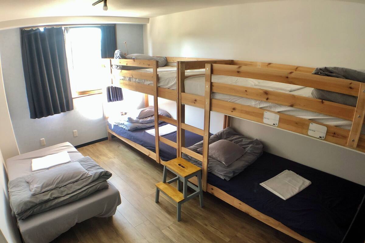 A dormitory room with bunk beds, a small table, and a window with curtains.
