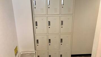 A row of beige metal lockers with handles, a white trash bin, and a yellow sign on the wall.