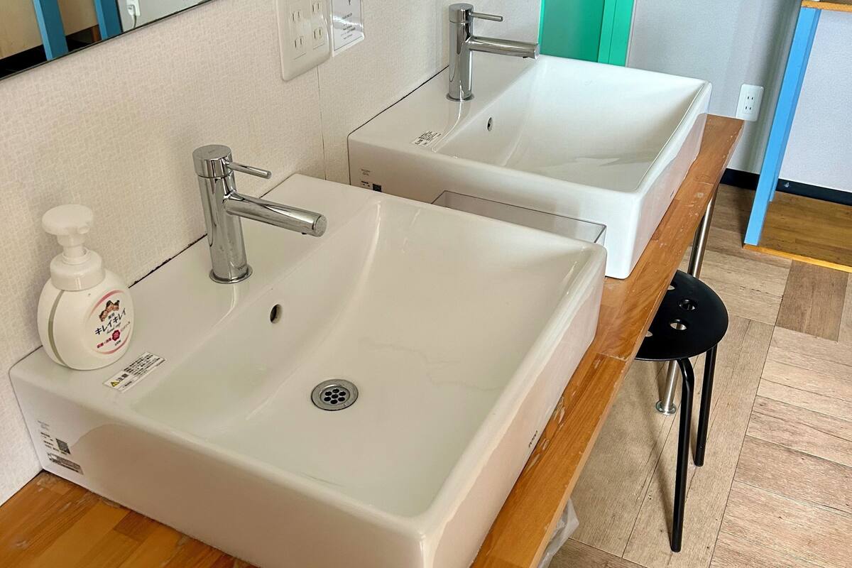 A bathroom with two sinks, a mirror, a soap dispenser, and a black stool.