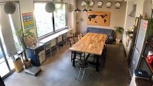 Cozinha moderna com mesa de madeira, cadeiras e forno embutido. Há plantas em vasos, um mapa-múndi na parede e um relógio mostrando as horas.