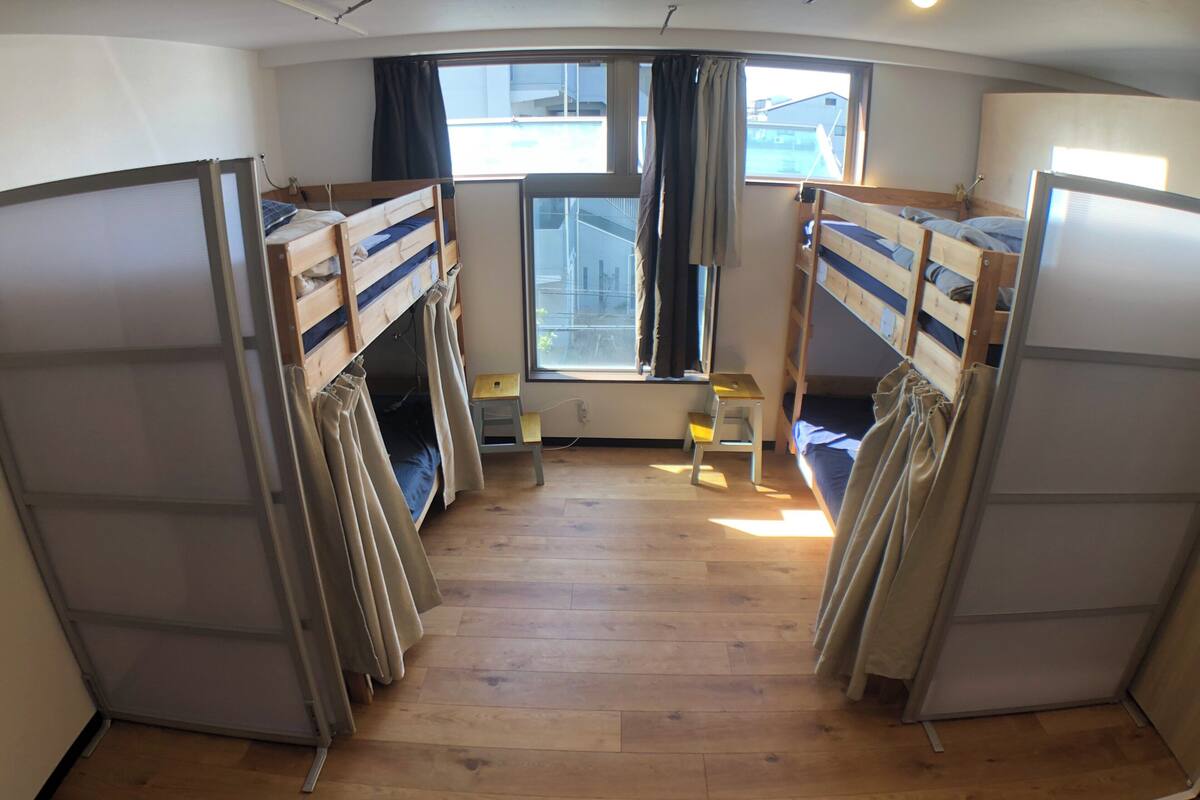 A dormitory room with bunk beds, a small table, and a window with curtains.