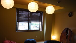 Quarto com esteiras de tatame, três bean bags, uma escultura de madeira e lanternas de papel.