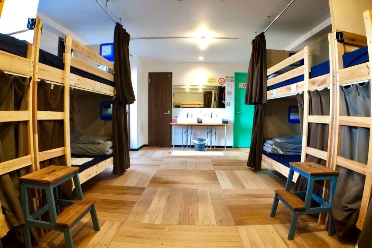 A dormitory room with bunk beds, a small desk, and a bathroom in the background.