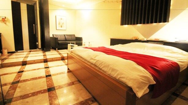 A hotel room with a checkered floor, a bed with a red blanket, a desk with a lamp, and a painting on the wall. - Hotel Bibi - Adults Only (Kashiba)