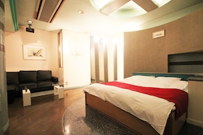A hotel room with a bed, a sofa, a small table, and a wall-mounted TV. - Hotel Bibi - Adults Only (Kashiba)