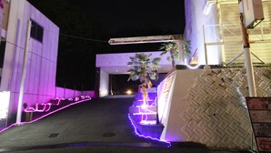 A building entrance with a staircase, a palm tree, and illuminated signage. - Hotel Bibi - Adults Only (Kashiba)
