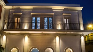 A two-story building with a balcony, arched doorways, and illuminated windows. - Palazzo Bove (Galatone)