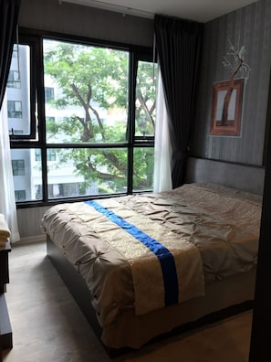 A bedroom with a large window, a bed with a beige and blue bedspread, and a tree outside.