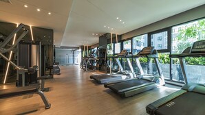Une salle de sport moderne équipée de tapis de course, d’appareils de musculation et dotée d’une grande fenêtre donnant sur un panorama urbain.