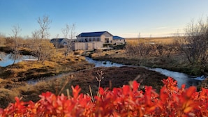 A rustic wooden building with a metal roof, situated beside a small stream in a natural landscape.