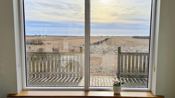 A room with a large window offering a view of a dry, open field.