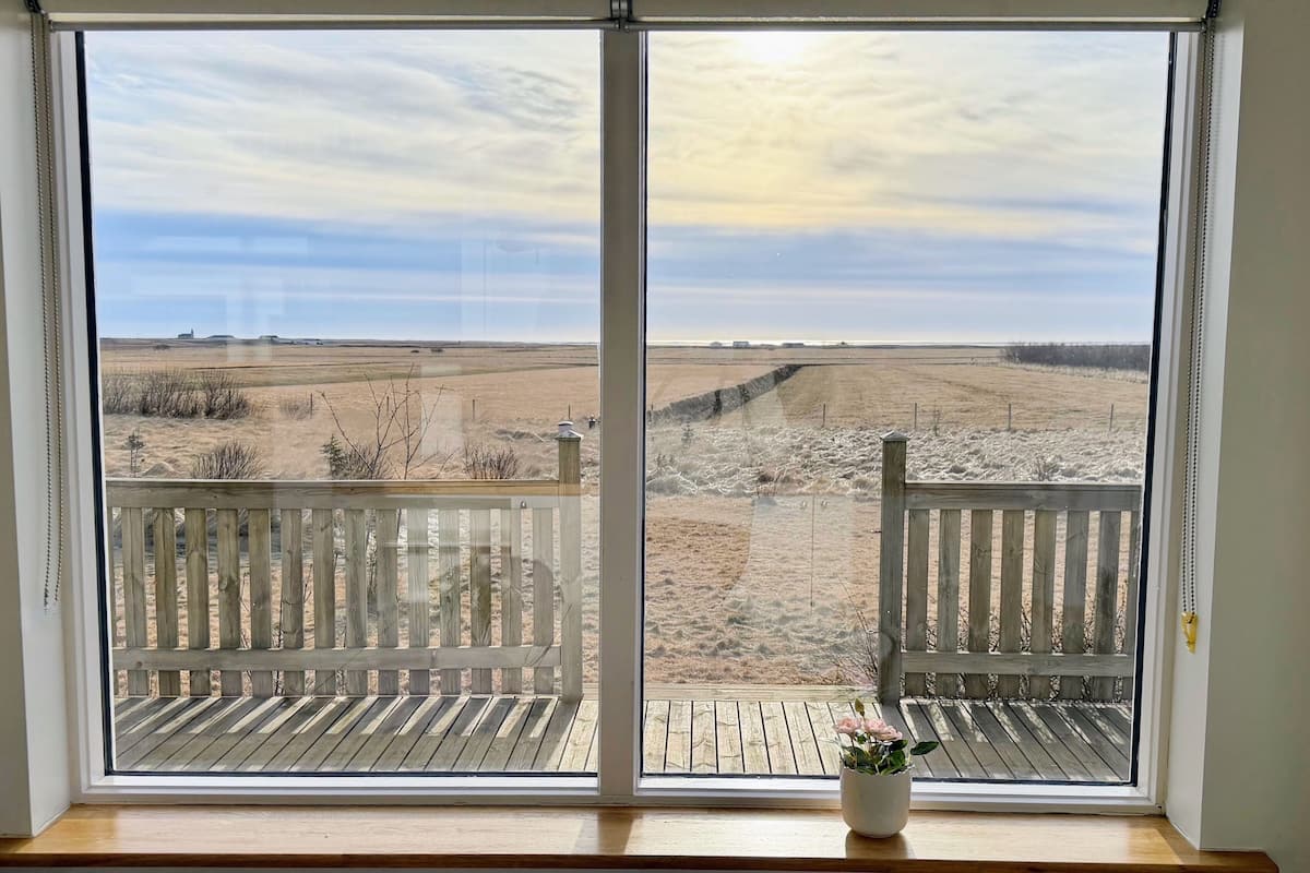 Ein Zimmer mit großem Fenster und Blick auf ein trockenes, offenes Feld.