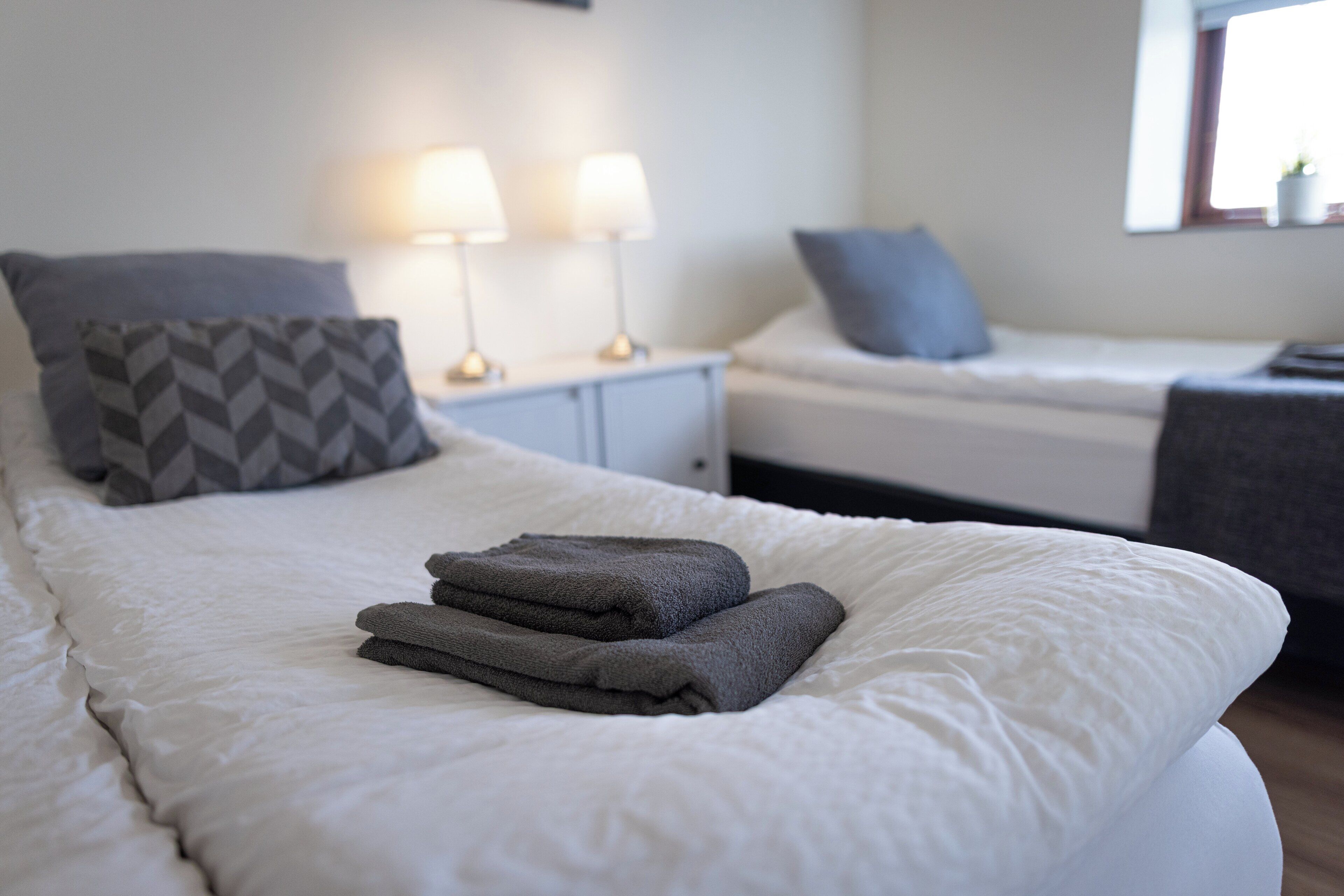 Een keurig opgemaakt bed met opgevouwen handdoeken, een nachtkastje met lampen en een raam met uitzicht.
