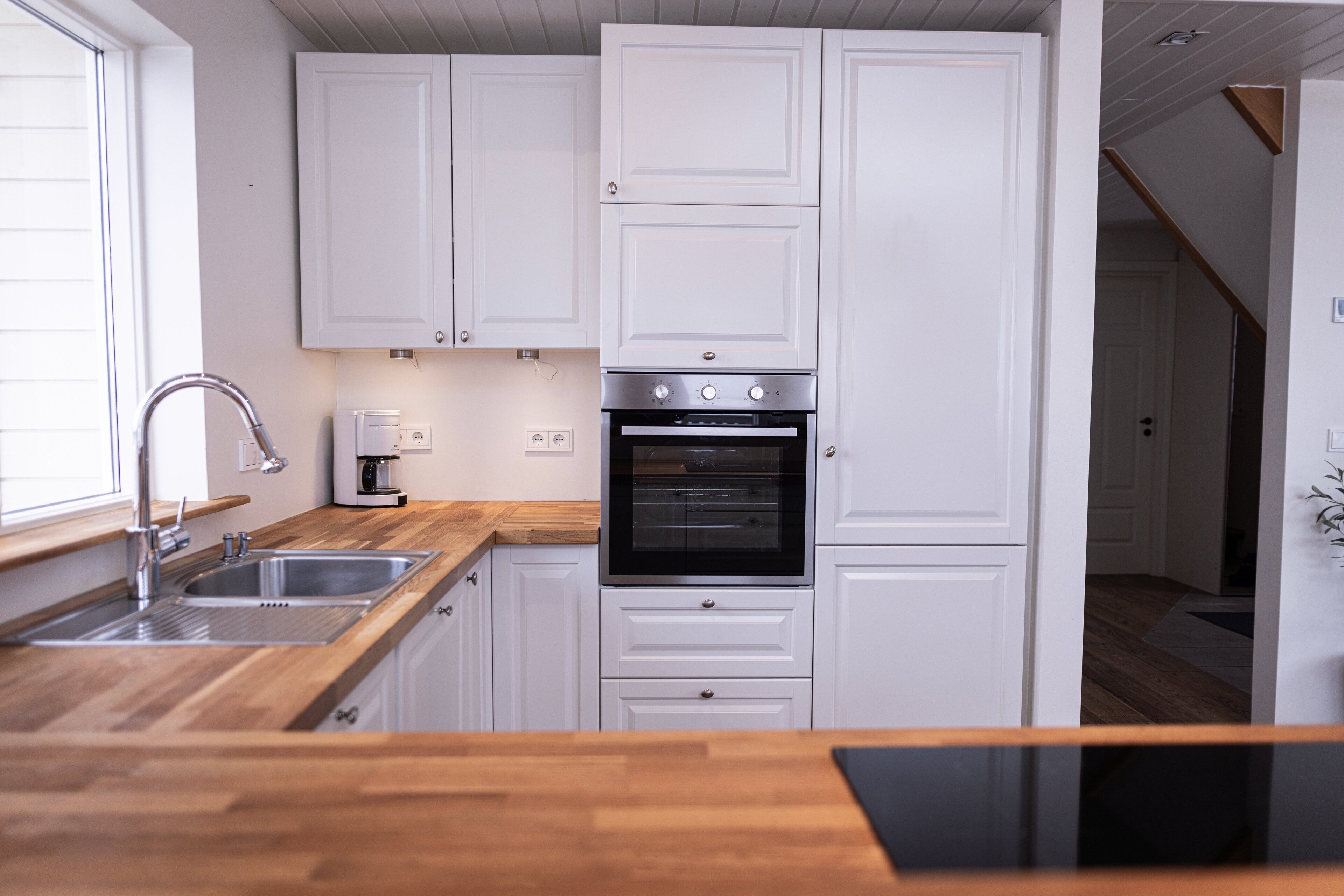 A kitchen with white cabinets, a stainless steel sink, a built-in oven, and a wooden countertop.