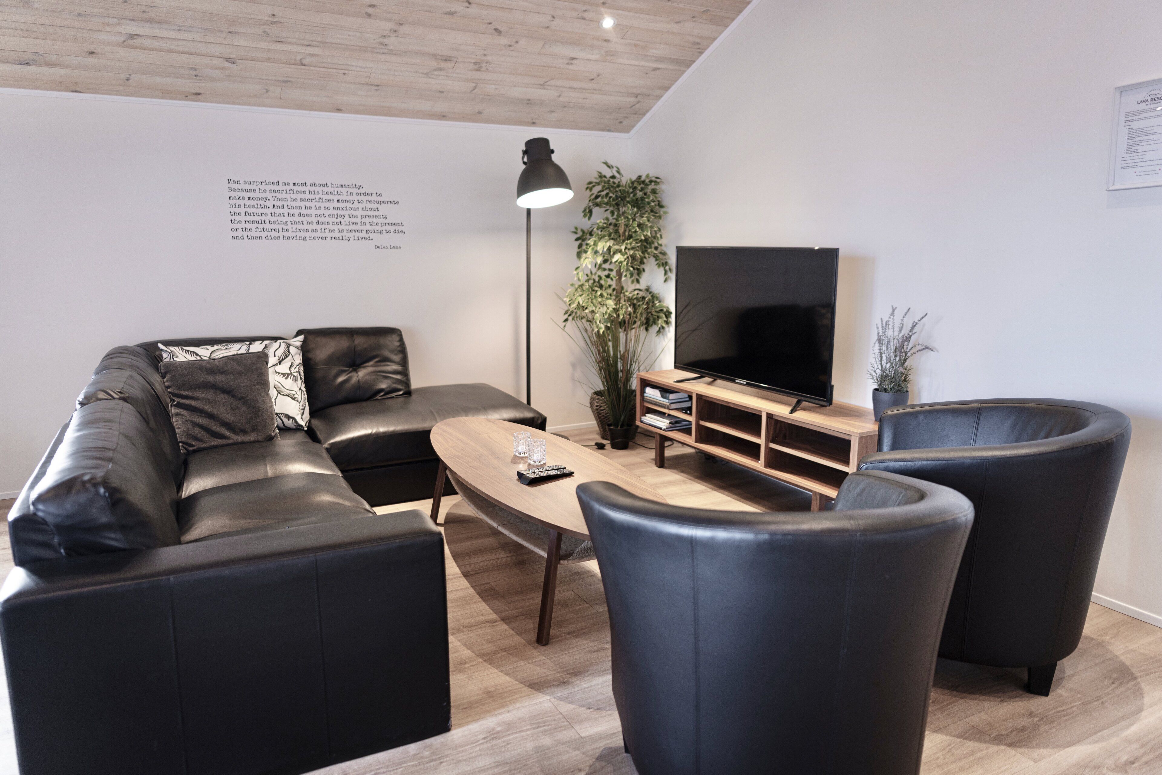 Una sala de estar moderna con un sofá de cuero negro, una mesa de centro de madera y un televisor de pantalla plana.