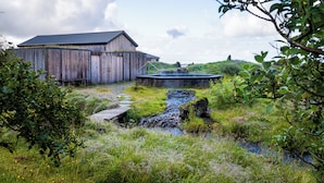 A rustic wooden building with a stone pathway leading to a small stream.
