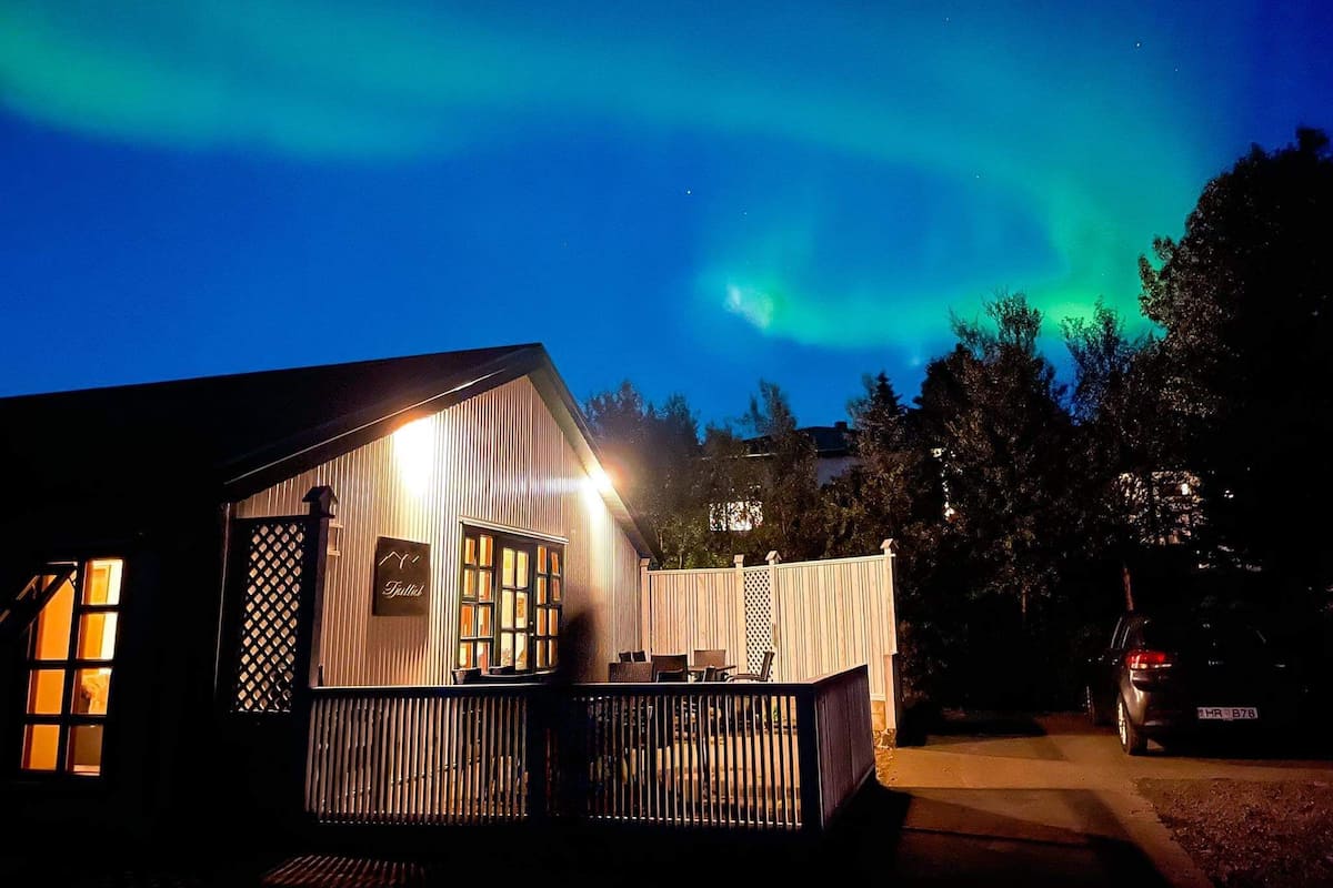 Eine Hütte mit Terrasse, einem beleuchteten Innenraum und Blick auf das Nordlicht.