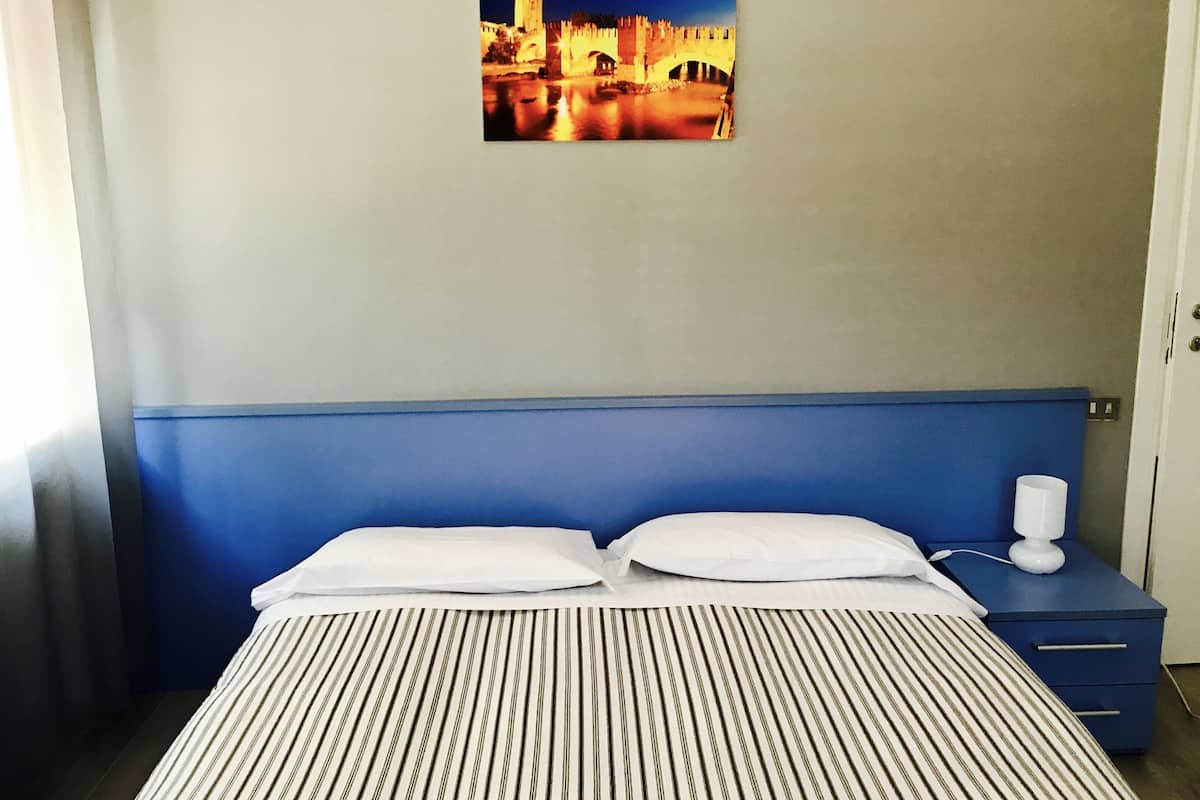 A hotel room with a bed, a nightstand, a lamp, and a framed picture of a cityscape on the wall.