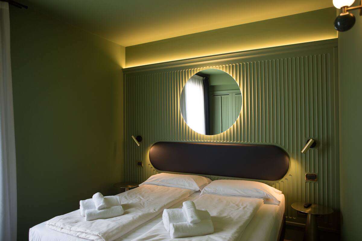 Una habitación de hotel con una cama grande, un espejo redondo y una mesita de noche pequeña.