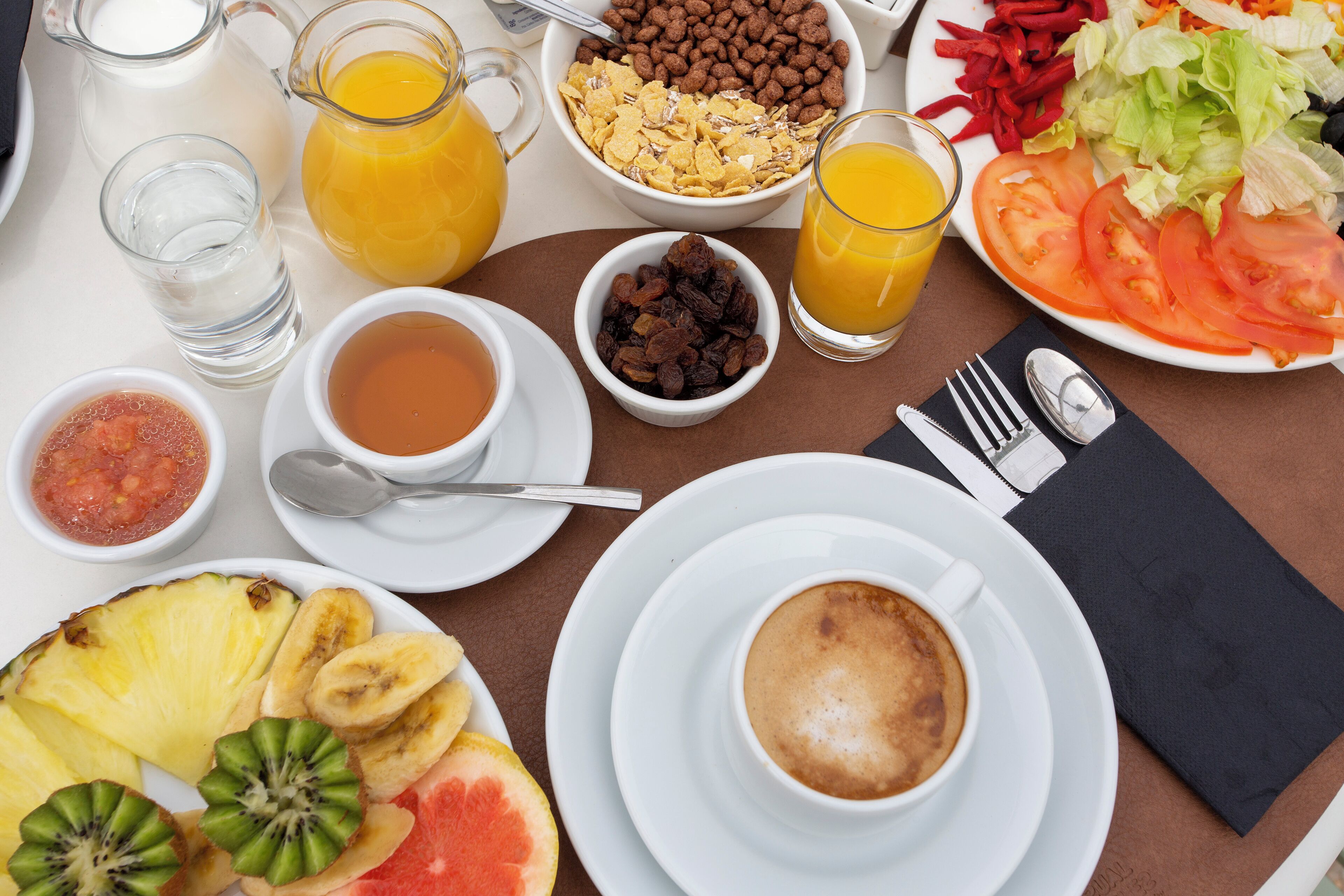 Een ontbijttafel met diverse etenswaren, drankjes en een kop koffie.