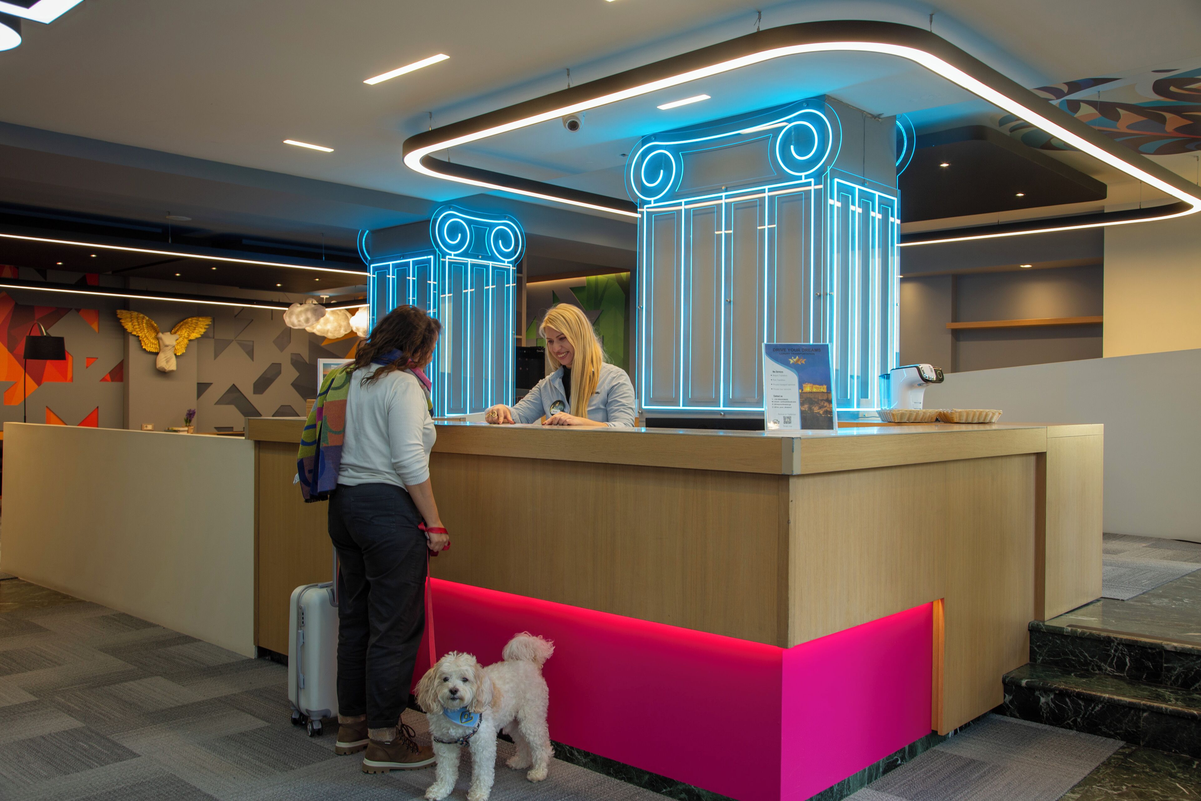 A hotel reception area with a wooden counter, a neon sign, and a small dog.