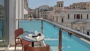 Un balcon avec une table ronde et deux chaises, donnant sur une piscine et des bâtiments historiques.