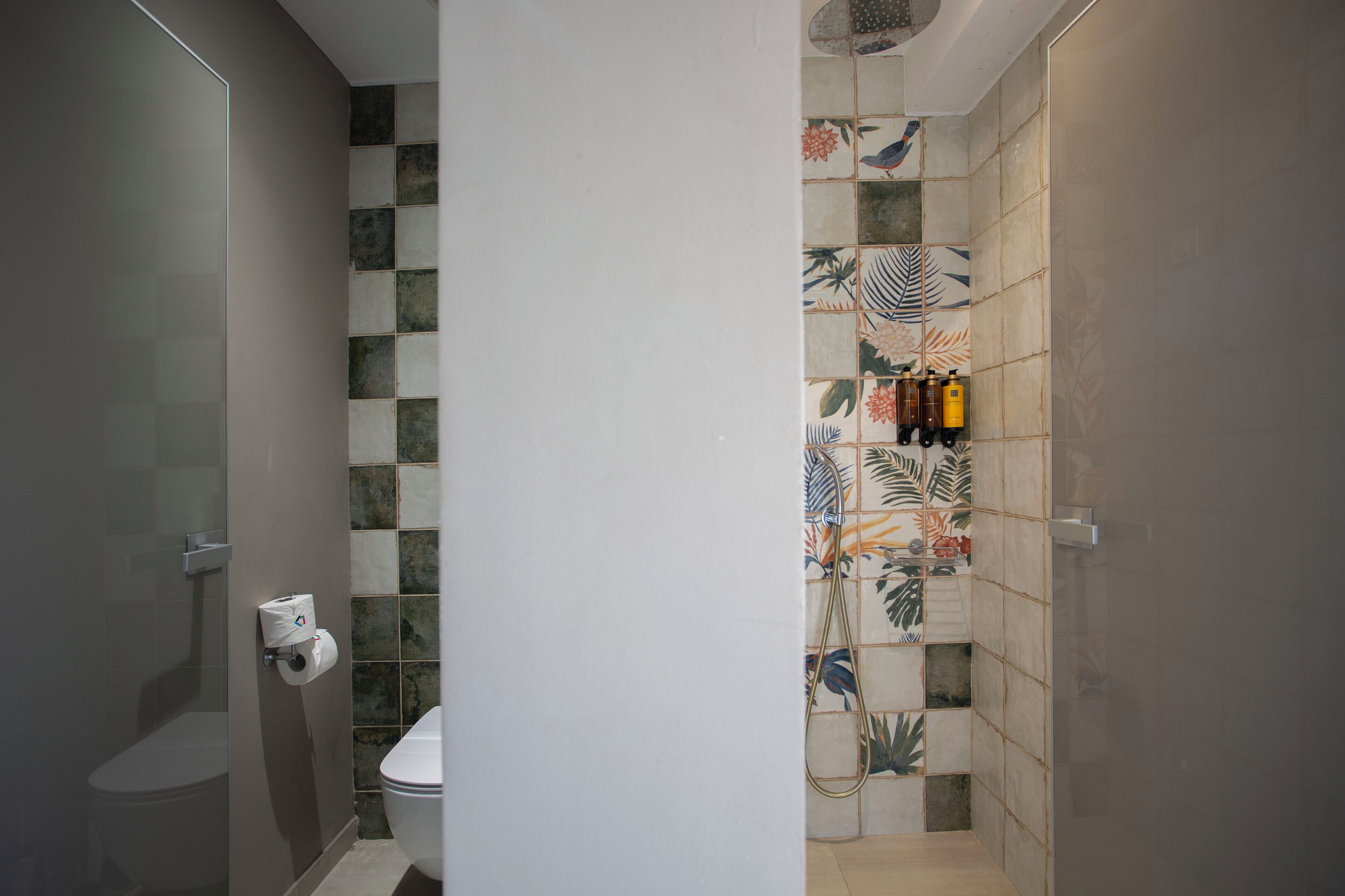 Un baño con inodoro, ducha con puerta de vidrio y pared con diseño de hojas.