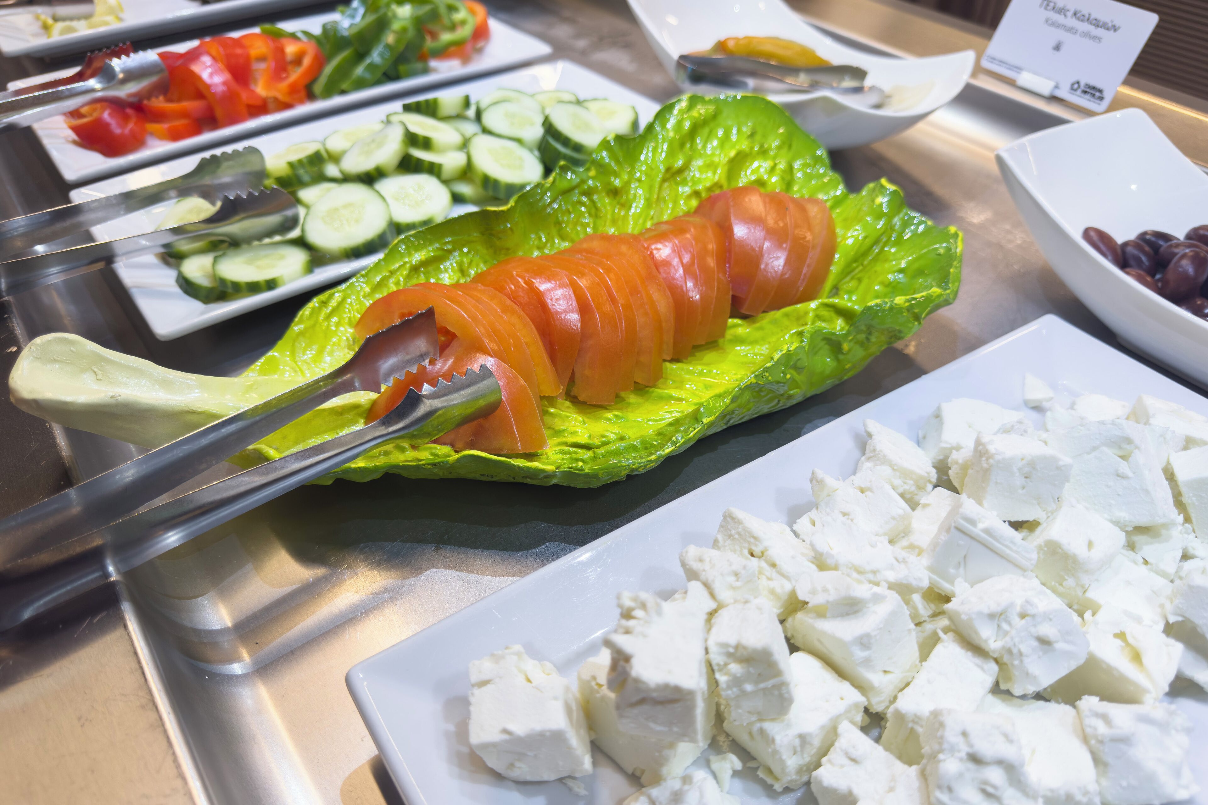 Un bufé con diversos alimentos, entre ellos pepinos en rodajas, tomates, lechuga y queso.