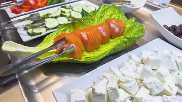 Un bufé con diversos alimentos, entre ellos pepinos en rodajas, tomates, lechuga y queso.
