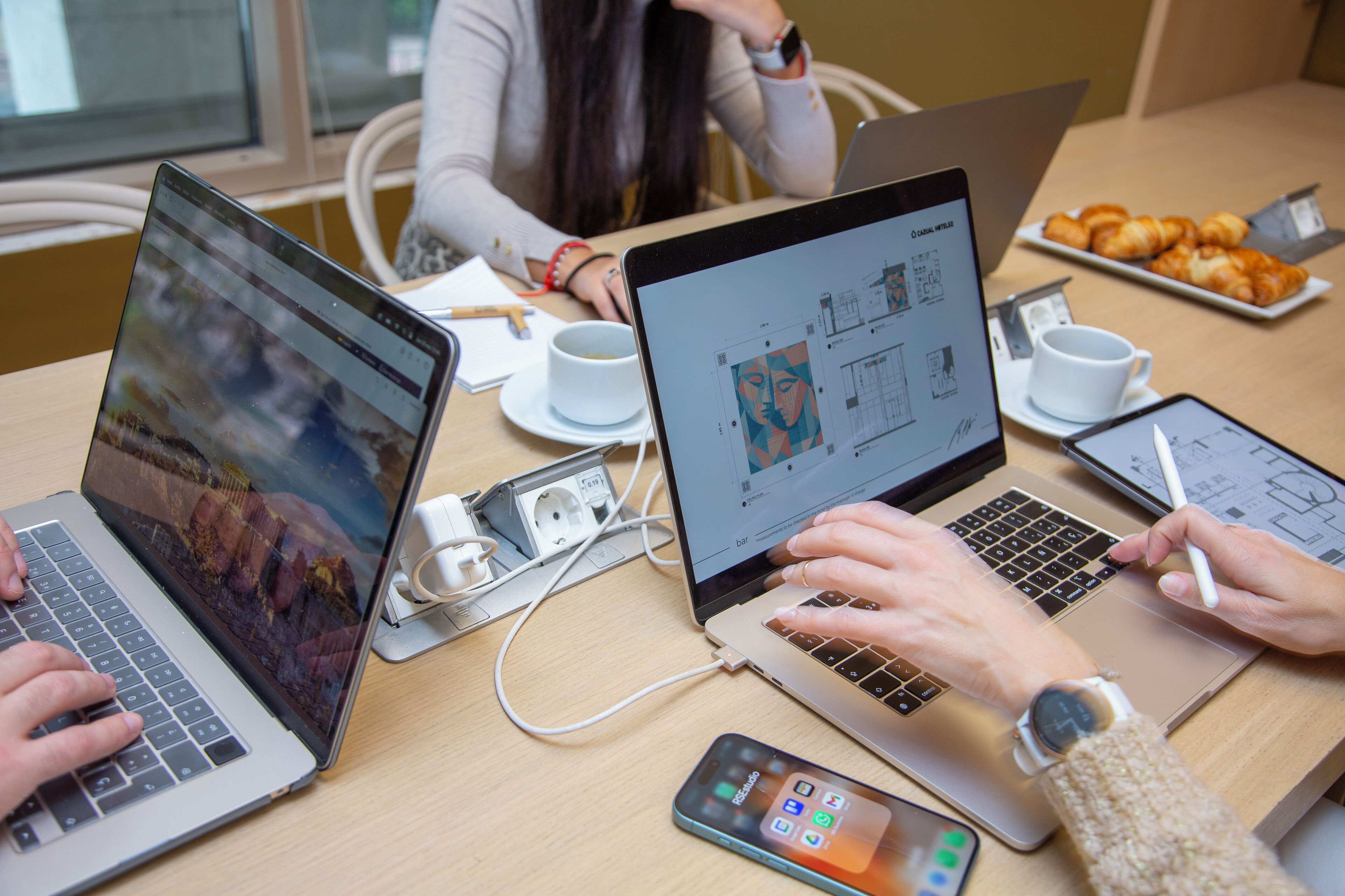 A meeting with laptops, smartphones, and a plate of pastries on a table.