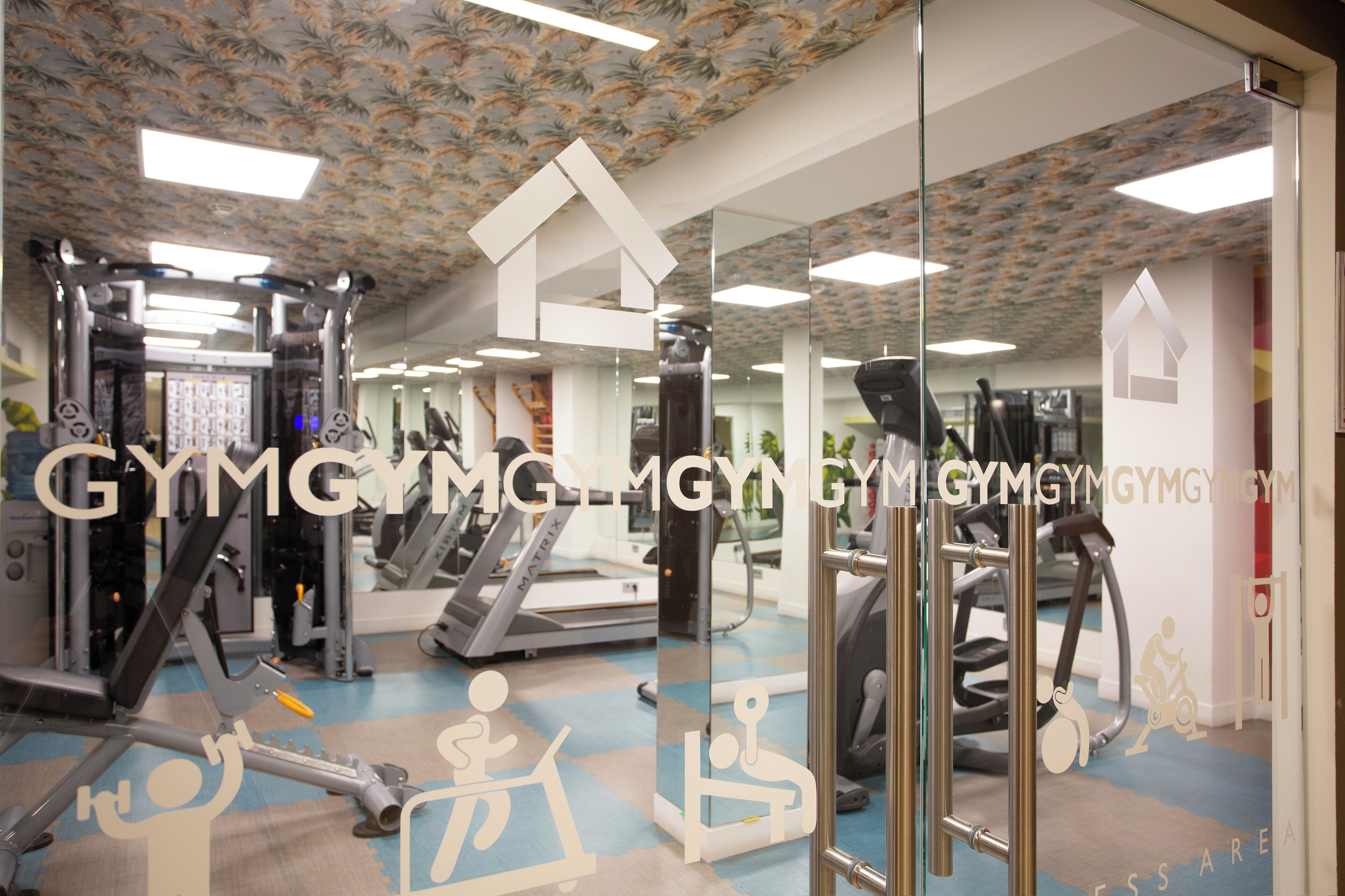 A gym with exercise equipment, mirrored walls, and a patterned ceiling.