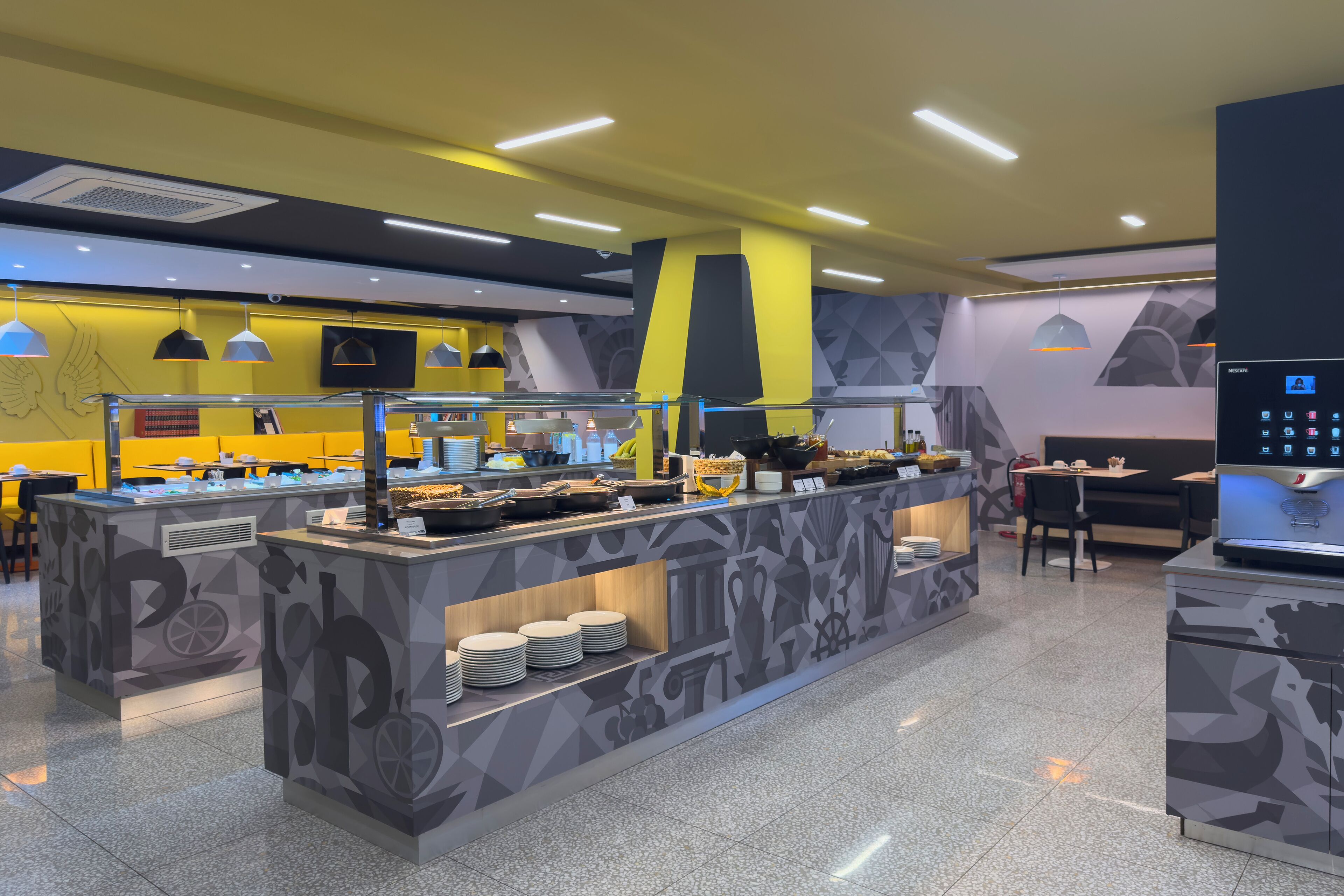 Uma área de buffet com um balcão central de serviço, diversas opções de assento e um design moderno com padrões geométricos.