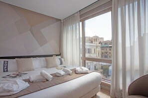 Hotellihuone, jossa on suuri sänky, ikkunasta avautuva näkymä kaupunkiin ja kaupunkimaisema, joka on nähtävissä ulkona.
