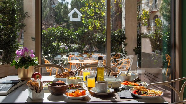 Une table de petit-déjeuner avec différents plats, un livre et une vue sur la ville par la fenêtre.