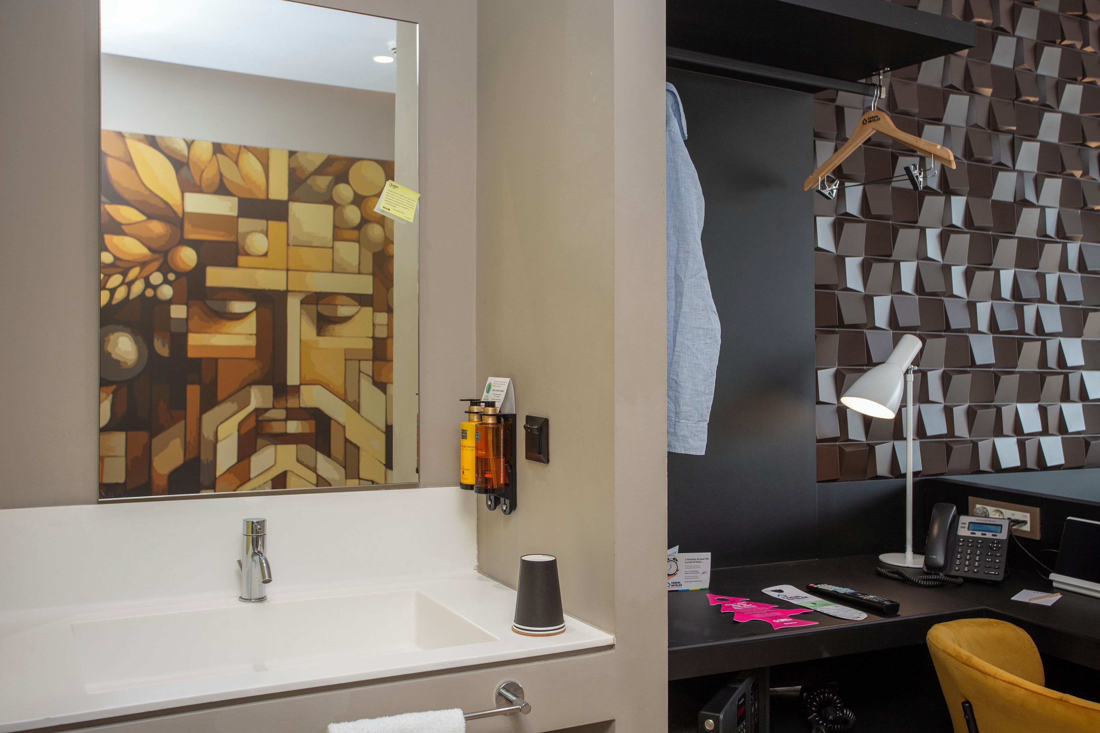 Un baño moderno con un lavamanos blanco, un espejo, un perchero para toallas, un escritorio con silla y un revestimiento de pared estampado.