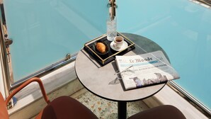 Un balcon avec une balustrade en verre donnant sur une vue panoramique de la ville, une table avec un journal, un croissant et une tasse de café.