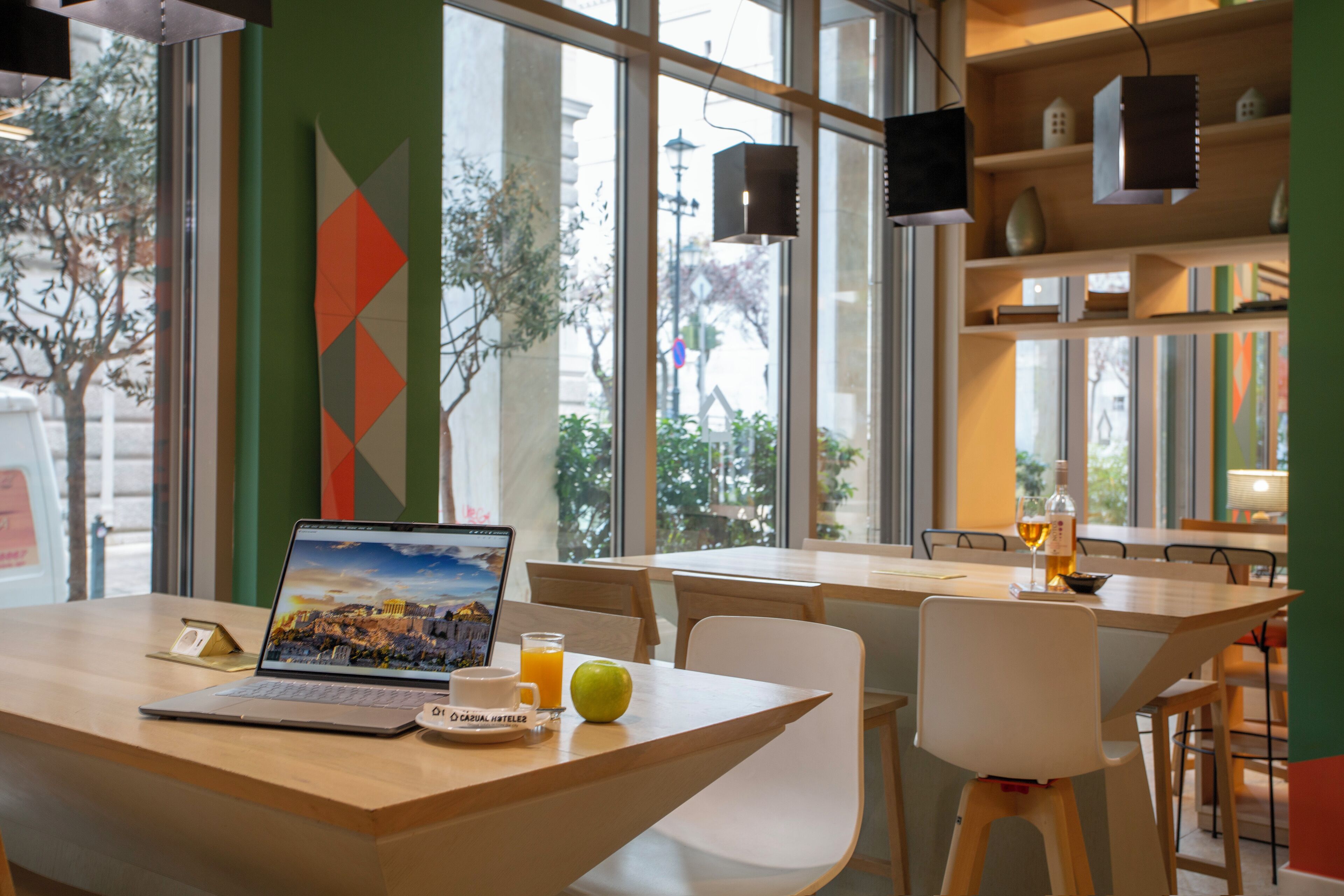 A modern cafe with a laptop on a table, a glass of orange juice, and a green apple.