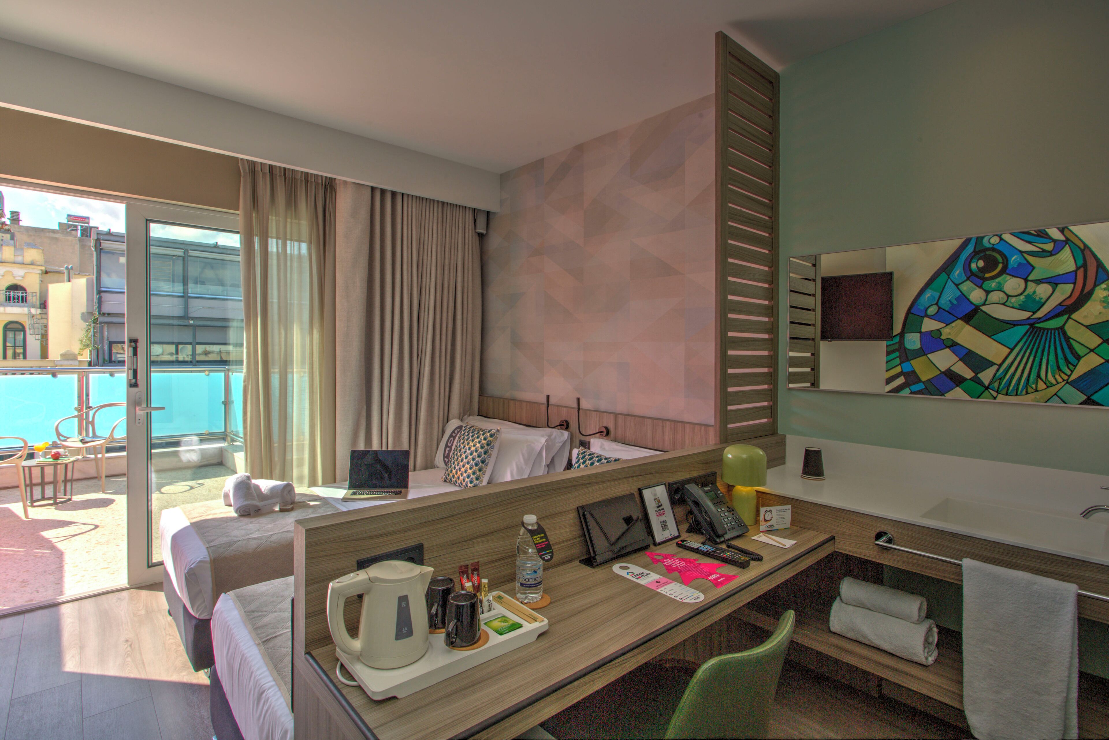 A hotel room with a bed, a desk with a laptop, a phone, and a window with curtains.