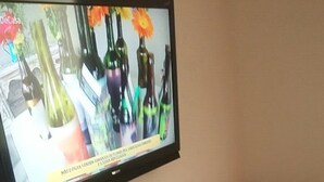 A television mounted on a wall, a bed with a leopard print bedspread, and a remote control on a table. - Studio Maximo (Rio de Janeiro)